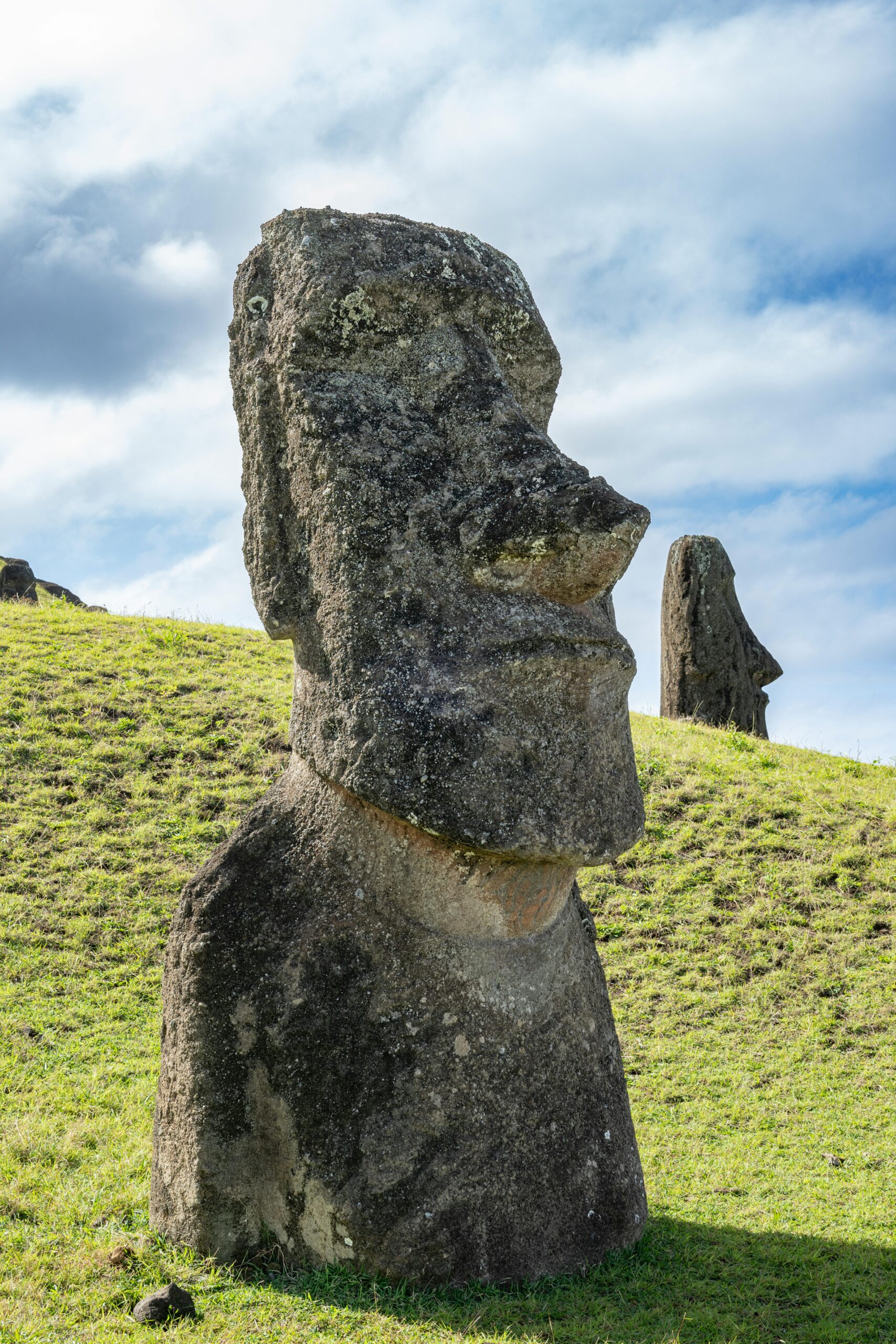 Historic Moai statue standing peacefully on grassy hill under a bright blue sky in Easter Island, Chile.
